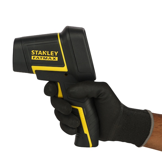 Photo of STANLEY FMHT0-77422 infrared thermometer held in a gloved hand, side angle, black and yellow body.