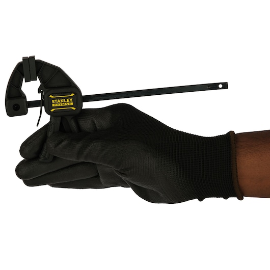 STANLEY FMHT0-83231 bar clamp held by a gloved hand, side angle, black and yellow design.