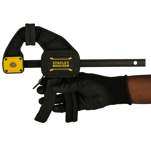 STANLEY FMHT0-83234 photography of a FATMAX bar clamp held in a gloved hand, side angle, black and yellow.