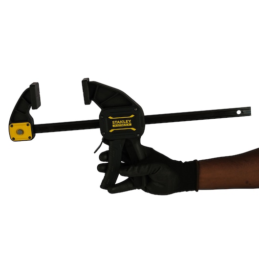 Photo of STANLEY FMHT0-83235 trigger clamp held in a gloved hand, black and yellow, side angle.
