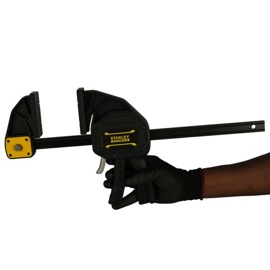 Stanley FMHT0-83239 trigger clamp held in gloved hand, side angle on white background.