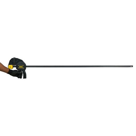 Stanley FMHT0-83242 bar clamp in black and yellow, side angle, held by gloved hand, white background.