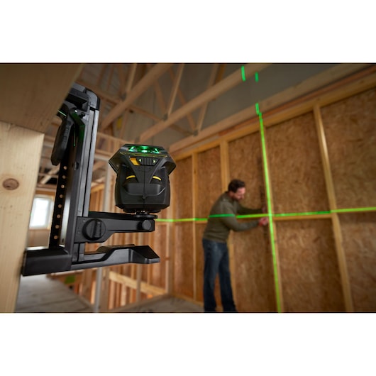 STANLEY FMHT1-77356 laser level projecting green lines on wall in construction site, side angle view.
