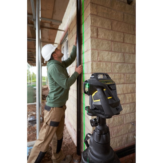 STANLEY FMHT1-77356 rotary laser level projecting green line on wall at construction site, worker aligning beam.