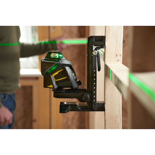 STANLEY FMHT1-77356 laser level projects green lines in a construction setting, mounted on a vertical support.