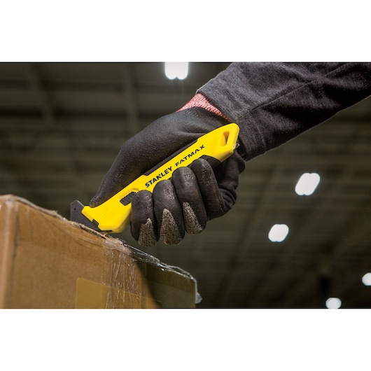 STANLEY FMHT10358-0 utility knife with yellow handle cutting box, shown held in gloved hand.
