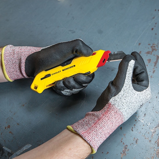Photo of STANLEY FMHT10362 utility knife with yellow handle, being used by gloved hands on a work surface.