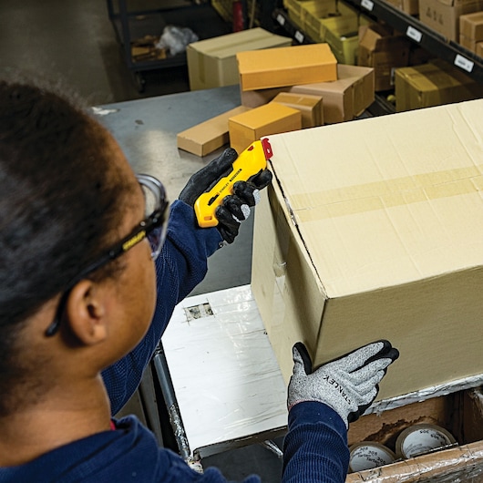 Photo of STANLEY FMHT10362 utility knife being used to open a cardboard box in a warehouse.