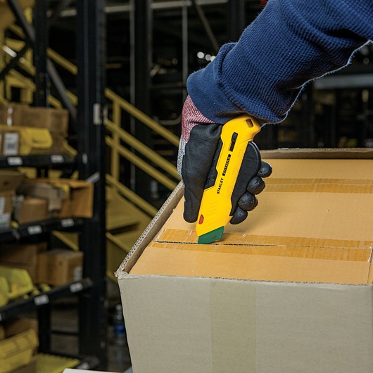 Stanley FMHT10363 utility knife used to cut tape on a cardboard box in a warehouse setting.