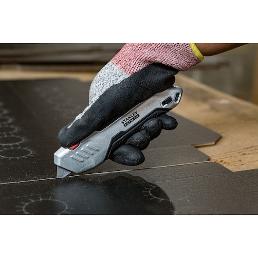 STANLEY FMHT10370-0 utility knife cutting cardboard, held by gloved hand, close-up photo.