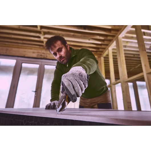 STANLEY FMHT10594-0 utility knife cutting sheet material, worker wearing gloves in construction setting.