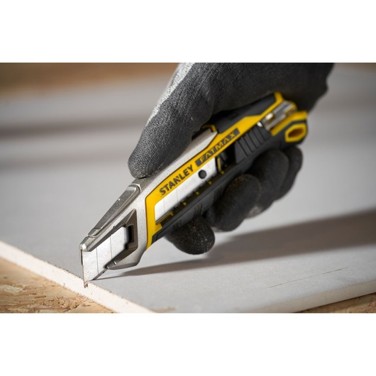 Photo of STANLEY FMHT10594-0 utility knife with yellow and black handle cutting drywall.
