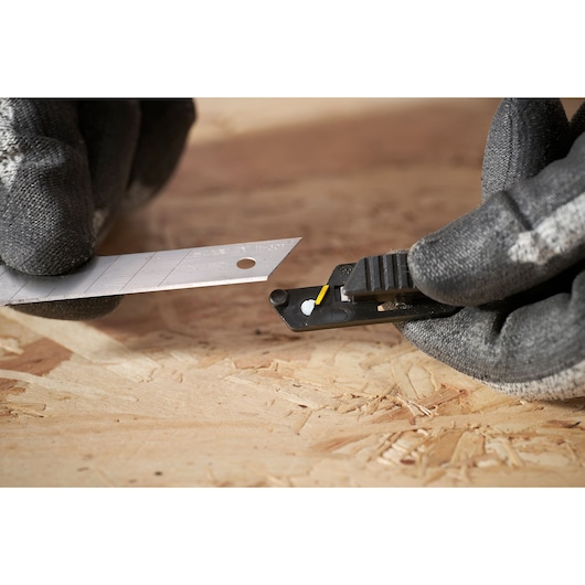 STANLEY FMHT10594-0 utility knife with segmented blade, close-up in use on wooden surface.