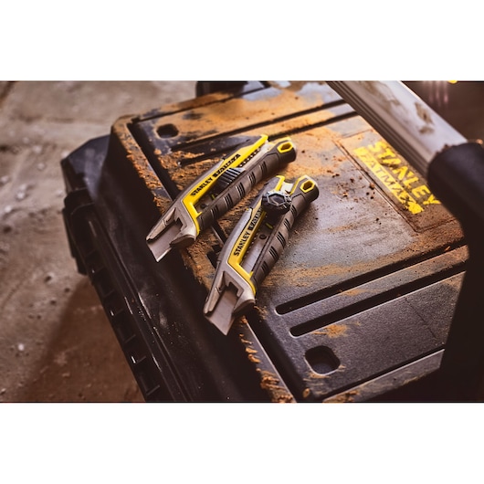 STANLEY FMHT10594-0 utility knives with yellow and black grip on a dusty tool box, angled view.
