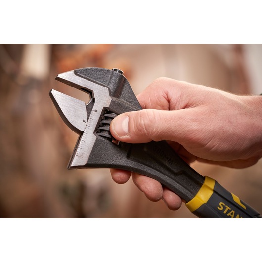 STANLEY FMHT13126-0 adjustable wrench held in hand, close-up on metal jaw and yellow-black handle.