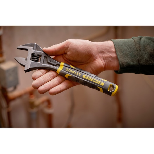 STANLEY FMHT13126-0 adjustable wrench with yellow and black handle, held in hand, shown in workshop setting.