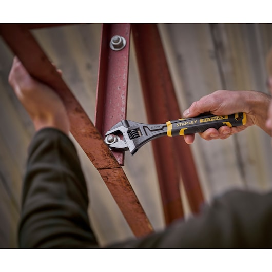 Stanley FMHT13127-0 adjustable wrench used to tighten bolt on red metal beam, close-up action shot.