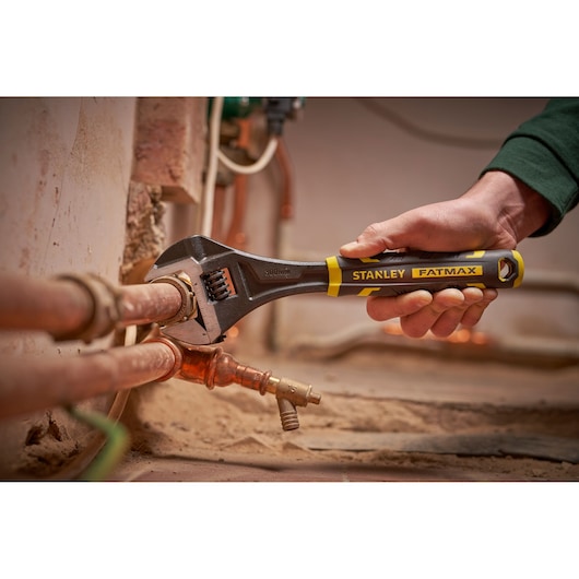 Photo of STANLEY FMHT13127-0 adjustable wrench being used on copper pipes, black and yellow handle.