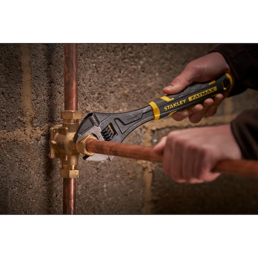 STANLEY FMHT13128-0 adjustable wrench turning pipe fitting against concrete wall.
