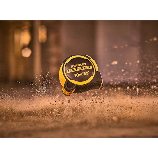 STANLEY FMHT33104-5 FATMAX tape measure, 10m/33ft, yellow and black, photographed mid-air with dust.