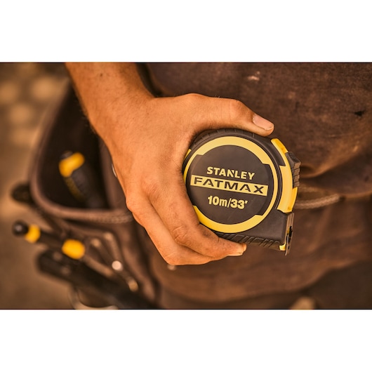 Photo of STANLEY FATMAX FMHT33104-5 tape measure 10m/33', yellow and black, held in a worker's hand.