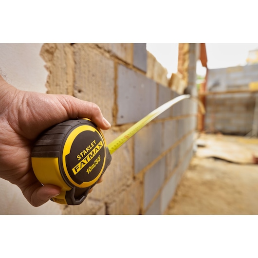 Photo of STANLEY FMHT33104-5 tape measure tool in hand, extending against a construction wall.