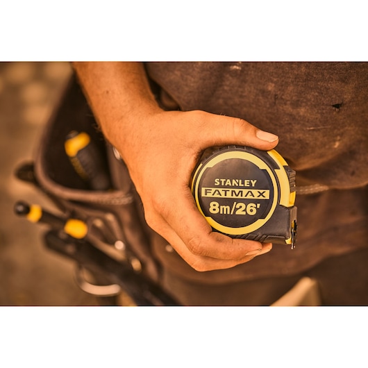 STANLEY FATMAX 8m/26' tape measure FMHT33105-5 held in hand, tool belt visible in background.