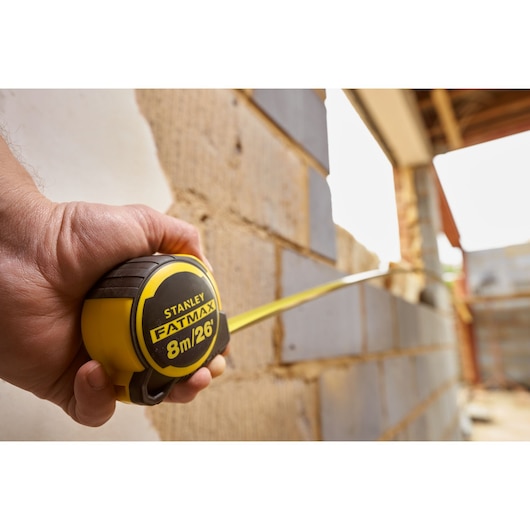 STANLEY FMHT33105 FATMAX tape measure 8m held in hand at construction site, yellow and black case.