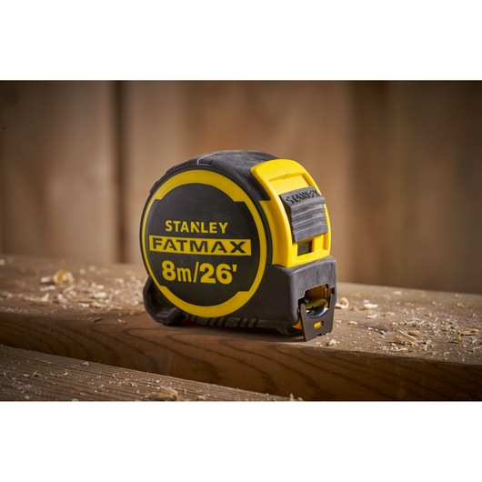 STANLEY FMHT33105 FATMAX tape measure 8m/26’ on wooden surface, yellow and black casing.