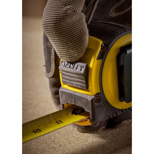 STANLEY FMHT33105 tape measure close-up, yellow and black, held by gloved hand.