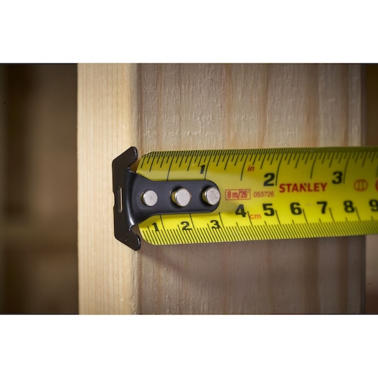 STANLEY FMHT33105 yellow tape measure extended, close-up side view against wooden surface.