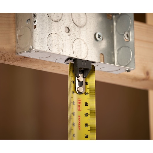 STANLEY FMHT33869 tape measure with yellow blade measuring wood and metal bracket close-up.