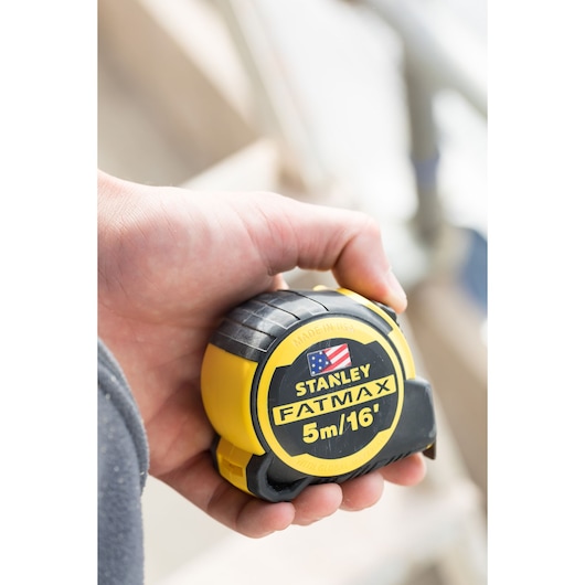 Photo of STANLEY FMHT36317-0 FATMAX tape measure, 5m/16ft, in hand, yellow and black casing.