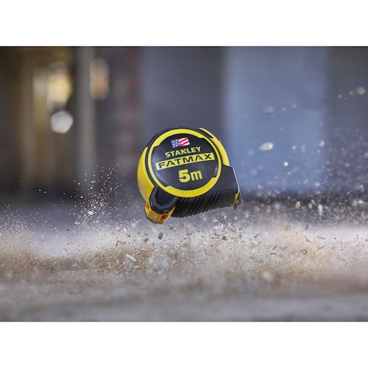 STANLEY FMHT36318-0 FatMax 5m tape measure in yellow and black, pictured falling on a dusty surface.