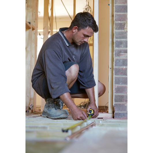 STANLEY FMHT36318-0 tape measure in use by a person measuring floor during construction.