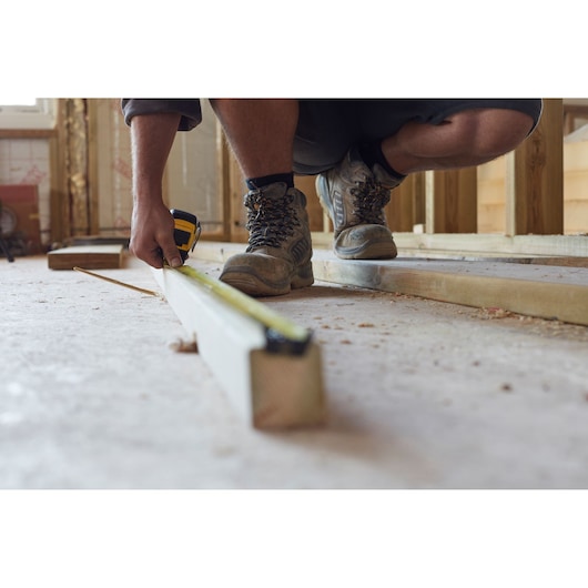 STANLEY FMHT36318-0 tape measure used on wood beam at construction site, close-up angle.