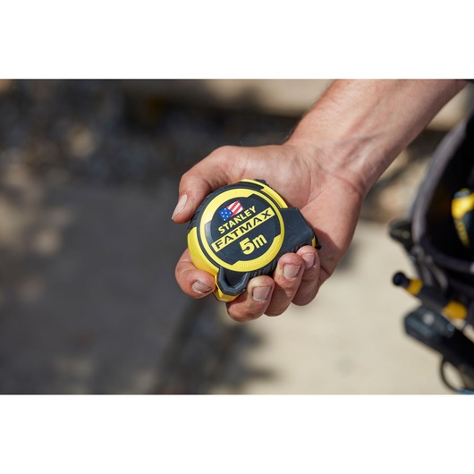 Photo of STANLEY FMHT36318-0 tape measure, yellow and black, held in a hand, product category photography.