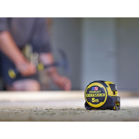 Photo of STANLEY FMHT36318-0 FATMAX 5m tape measure on carpeted floor, with blurred background.