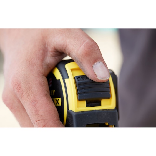 Photo of STANLEY FMHT36318-0 tape measure, close-up of thumb pressing black lock button.