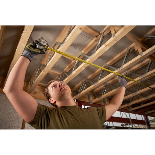 Photo of STANLEY FMHT38215-5 tape measure used by a person measuring wooden beams indoors.