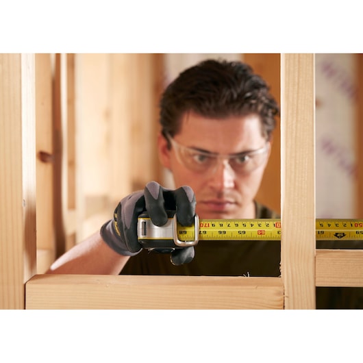 STANLEY FMHT38215-5 tape measure in use for wood framing, close-up view of yellow tape in gloved hand.