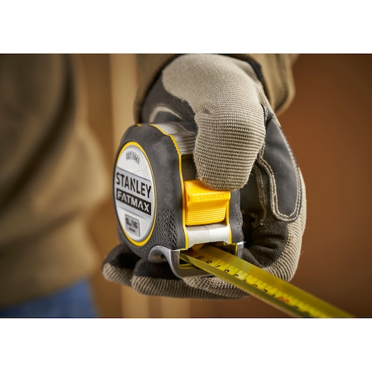 STANLEY FMHT38215-5 tape measure held by gloved hand, close-up, product photography.