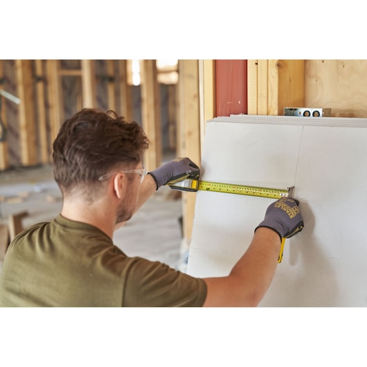 Photo of person using STANLEY FMHT38233-5 tape measure during drywall installation on construction site.