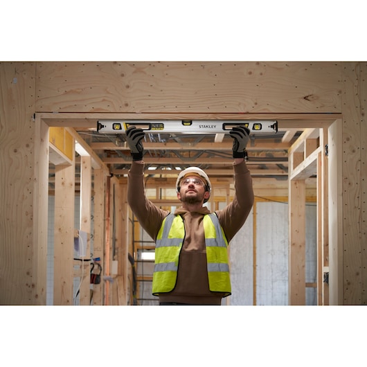 Photo of worker using STANLEY FMHT43674-1 spirit level in wooden construction, holding tool above head for alignment.
