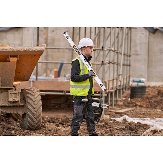 Photo of STANLEY FMHT43675-1 spirit level held by worker at construction site, yellow and black accents visible.