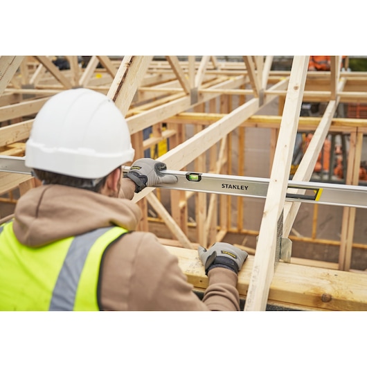 STANLEY FMHT43679-1 spirit level used by worker with gloves and hard hat on wooden roof construction site.