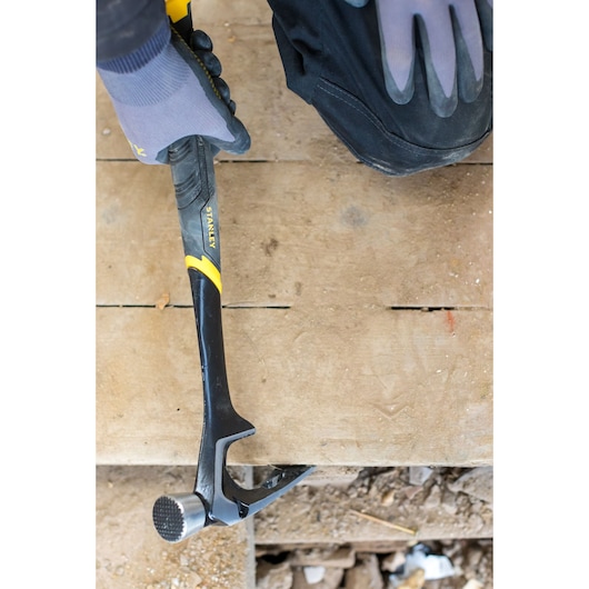 Photo of STANLEY FMHT51367-2 claw hammer in use on wood floor, black and yellow handle, shown with gloved hand.