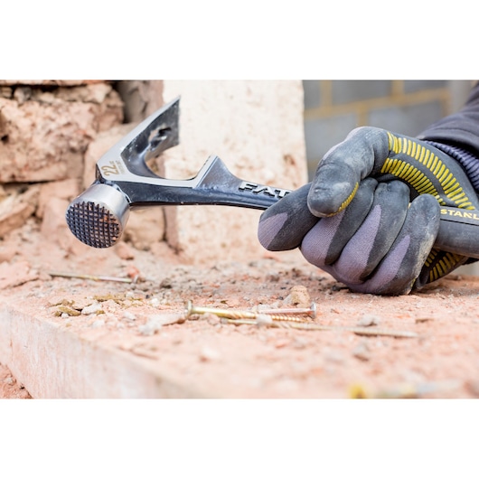 STANLEY FMHT51367-2 claw hammer held by gloved hand on construction site with bricks and screws.