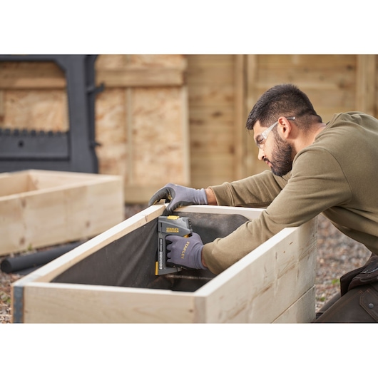 STANLEY FMHT6-70868 staple gun being used to fasten fabric inside a wooden planter box outdoors.