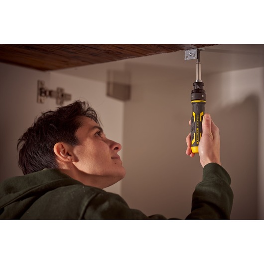 STANLEY FMHT62692-0 ratcheting screwdriver used inside cabinet, yellow and black handle visible.